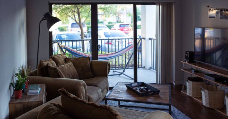 Inside the living room of a rental property overlooking a hammock on a balcony and common area parking lot.