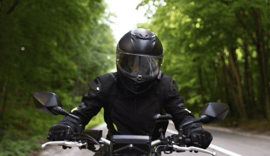 Motorcycle rider in full safety gear and a black helmet riding on a tree-lined road.